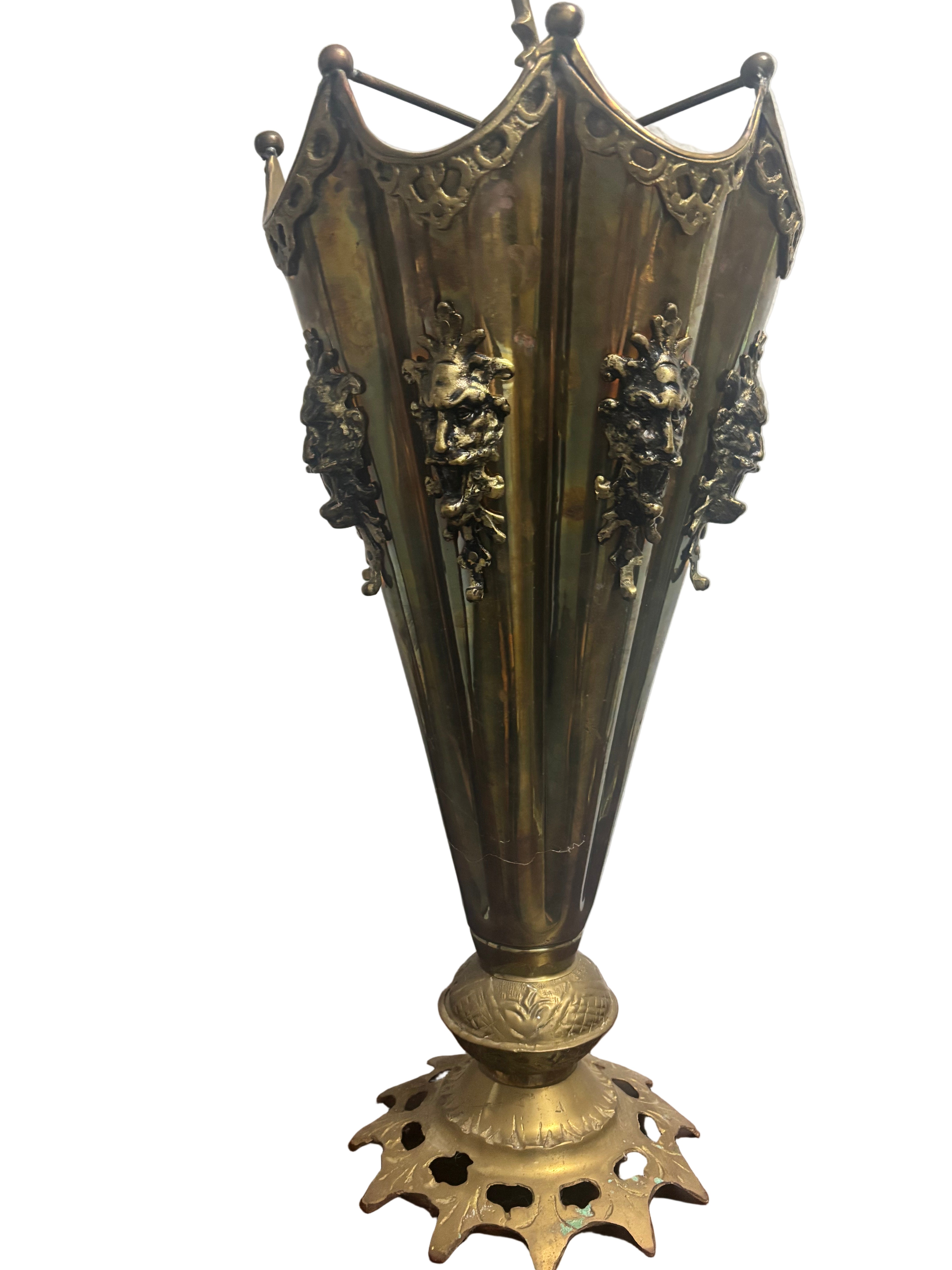 A decorative brass vase with a fluted design, ornate lion head accents, and a star-shaped base, resting on a wooden surface.