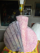 A decorative lamp with a shell-shaped base featuring a gradient of pink and lavender colors, sitting on a colorful patterned tablecloth.