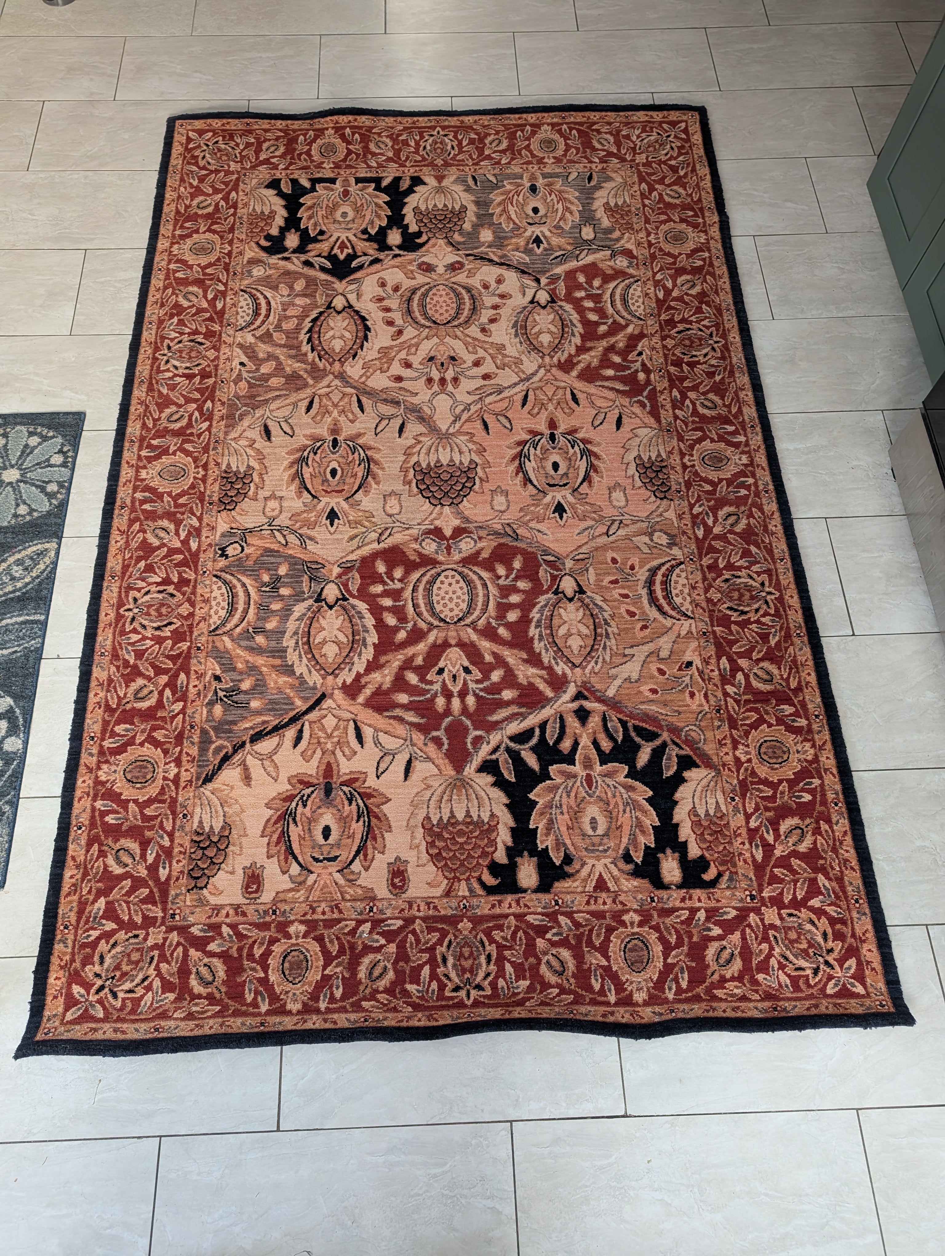 A decorative area rug features intricate floral patterns in warm reds, golds, and blacks, placed on a light tiled floor.