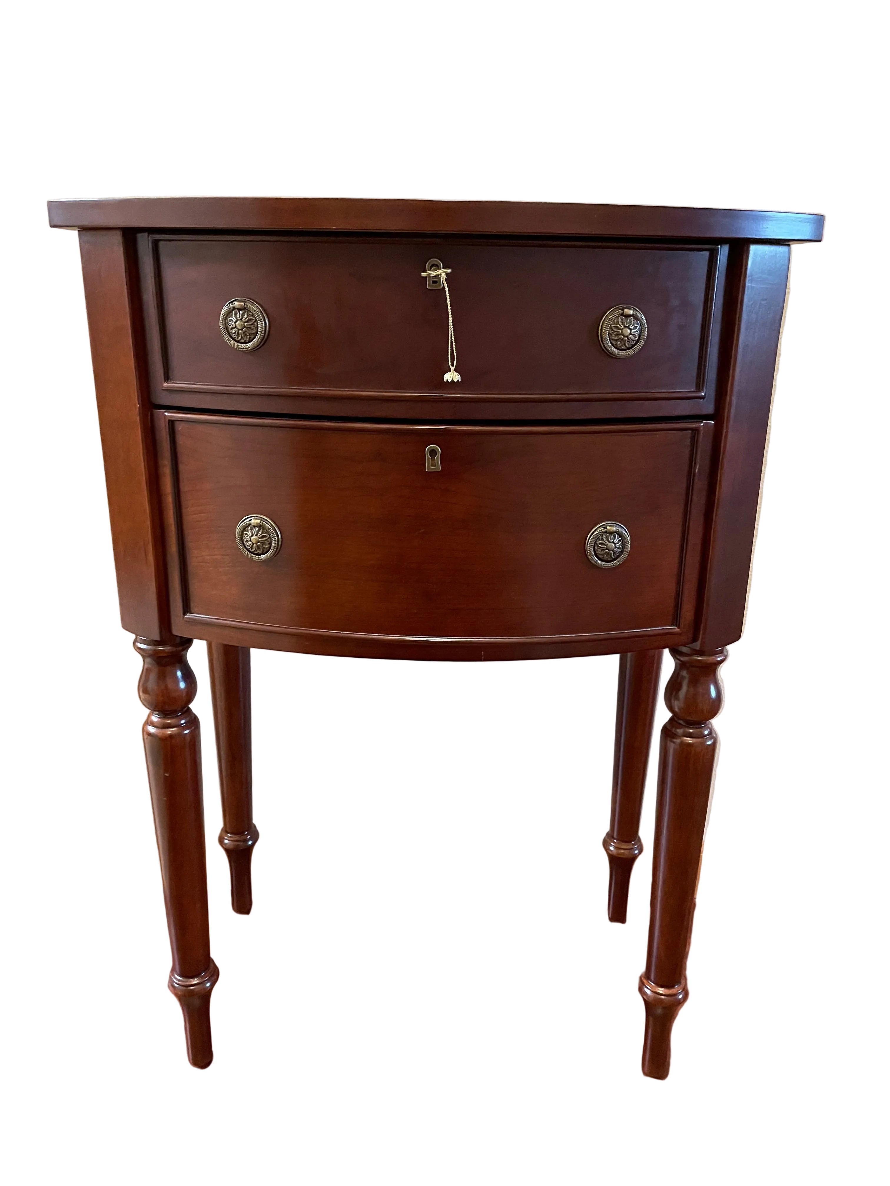 A classic wooden side table with two drawers, featuring ornate metal handles and curved legs, placed against a light-colored wall.