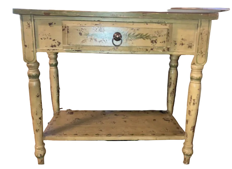 A vintage yellow side table with a single drawer, featuring worn paint and decorative detailing. It's positioned in front of a TV.
