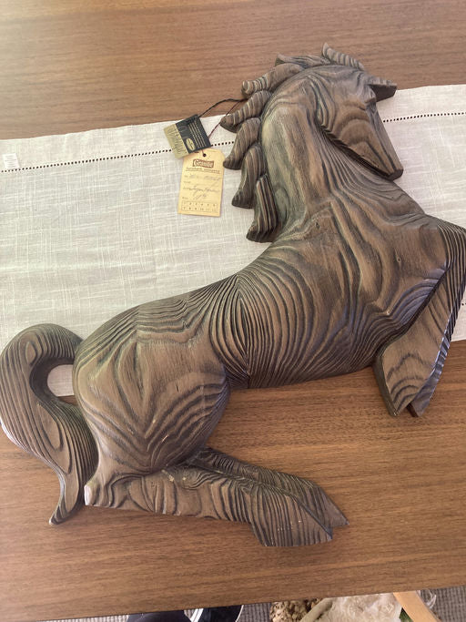 A wooden horse sculpture rests on a table, showcasing intricate grain patterns. A price tag is attached, indicating it is a decorative item.