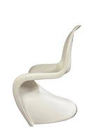 A modern white chair with a curved design is positioned in a garage setting, with wooden garage doors in the background and some cleaning tools nearby.