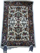 A floral-patterned rug featuring intricate designs in shades of cream, burgundy, green, and blue, laid out on a reflective surface.