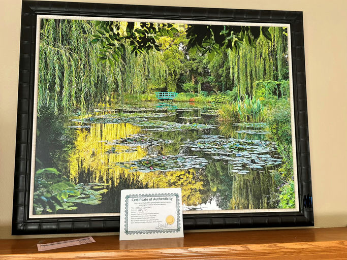 A vibrant landscape painting featuring a serene pond surrounded by lush greenery and water lilies, displayed alongside a certificate of authenticity.