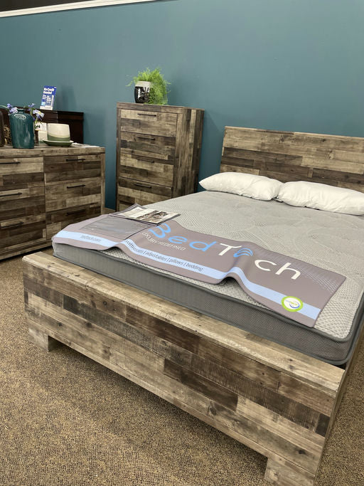 A wooden bed frame with a mattress labeled "BedTech" is showcased in a room with blue walls, complemented by matching dressers and decor.