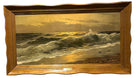 A seascape painting depicts waves crashing on a shore during sunset, with light reflecting off the water, framed in a wavy wooden frame.