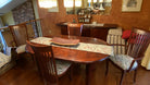 A cozy dining area featuring a wooden table with a decorative runner, surrounded by eight wooden chairs, and a hutch displaying teacups.