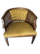 A vintage half-moon chair with a tufted mustard-yellow fabric seat and cane backrest, set on a light carpet, surrounded by household items.