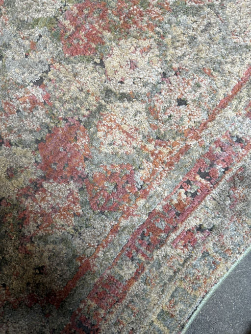 A close-up view of a colorful, patterned rug featuring intricate designs in shades of red, green, and beige with a textured surface.