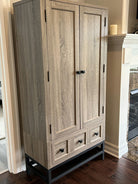 A wooden cabinet with a light oak finish and black hardware, featuring two doors and three drawers, stands against a wall in a cozy interior.