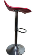 A modern red bar stool with a chrome base and footrest, set against a neutral wall with a closed door in the background. Floor is dark wood.
