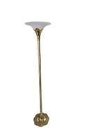 A tall, gold metal floor lamp with a wide, white shade stands in a garage with concrete flooring and a partially visible cardboard box nearby.