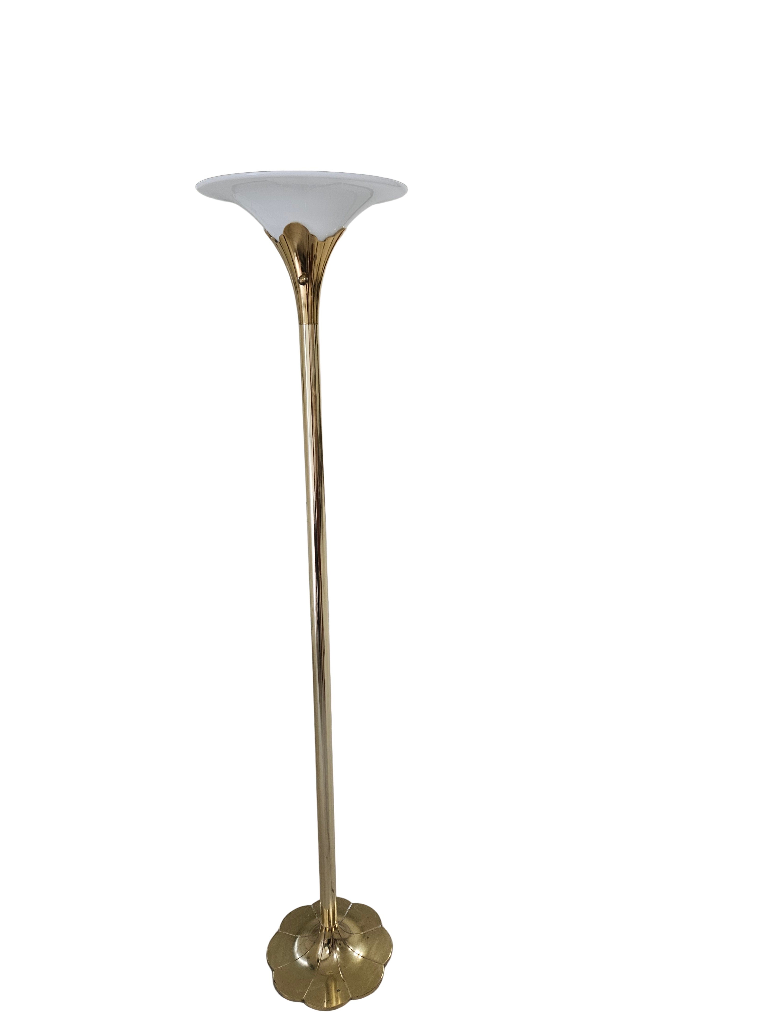 A tall, gold metal floor lamp with a wide, white shade stands in a garage with concrete flooring and a partially visible cardboard box nearby.