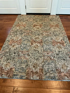 A textured area rug with a mix of blue, gray, and warm tones, placed on hardwood flooring in front of double doors.