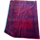 A red patterned rug is placed on a wooden floor, with a small corner showing frayed edges. A foot with red toenails is partially visible in the corner.