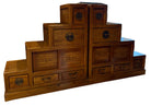 A wooden dresser with several drawers, displaying intricate designs, stands in a spacious room with hardwood floors and large windows.