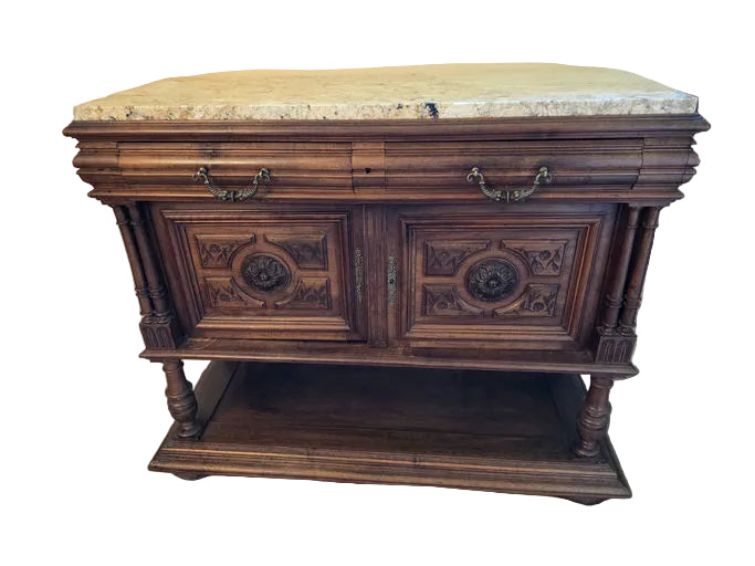 A wooden sideboard with ornate carvings and a marble top, featuring two cabinets with decorative doors and elaborate hardware, stands on a tiled floor.