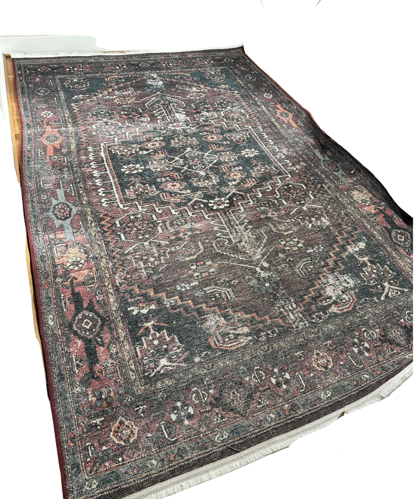 A richly patterned area rug with intricate designs in shades of red, blue, and gray, placed on a wooden floor in a bright room.