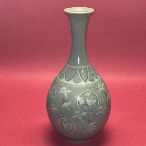 A tall, elegant vase with a narrow neck, featuring intricate designs of birds and clouds against a soft, gray background. Set against a pink backdrop.