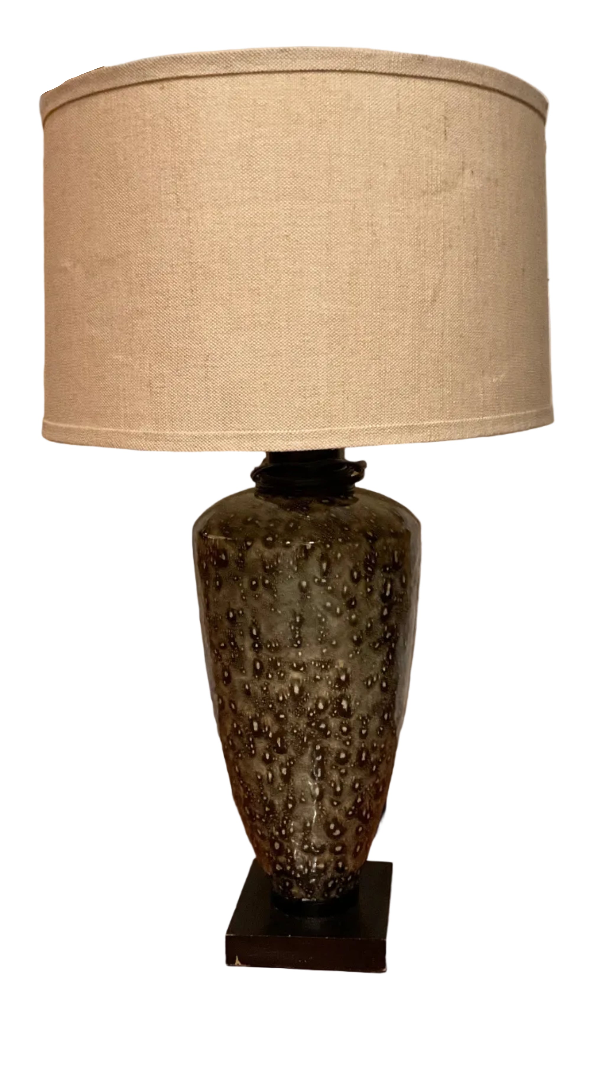 A decorative lamp with a patterned ceramic base and a beige fabric shade stands on wooden flooring next to a white door.