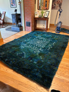 A plush, blue and green rug lies on wooden flooring in a cozy living room, featuring a brick wall, a vintage stove, and decorative items on a table.