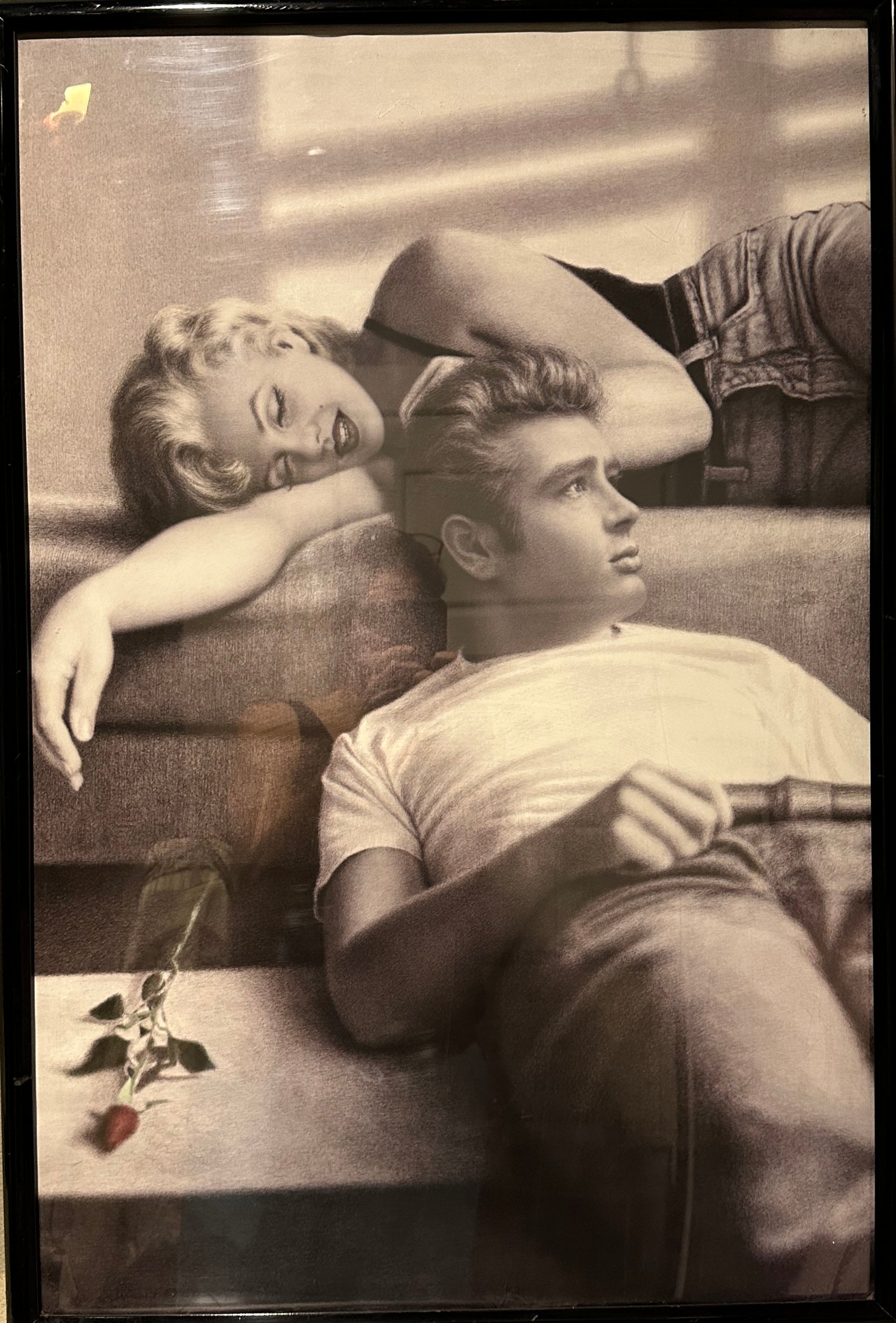 A black-and-white framed print features a smiling woman with blonde hair lounging beside a thoughtful man, a rose resting on the surface below.