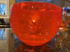 A bright red plastic bowl with decorative leaf patterns rests on a dark countertop, reflecting warm light and showcasing its glossy surface.