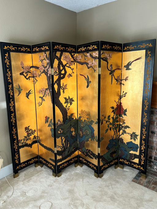 A decorative folding screen featuring intricate artwork of birds and flowers on a golden background, with black and gold accents.