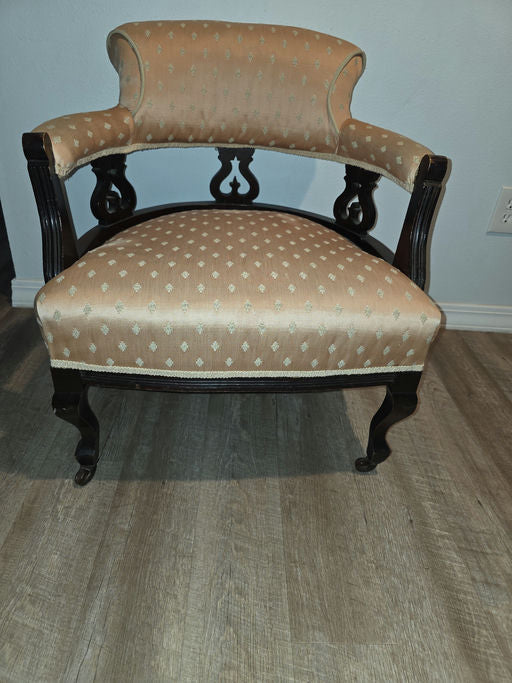 A vintage chair with a curved backrest and black wooden frame, upholstered in light orange fabric featuring a subtle pattern, placed on a wood floor.