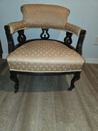 A vintage chair with a curved backrest and black wooden frame, upholstered in light orange fabric featuring a subtle pattern, placed on a wood floor.