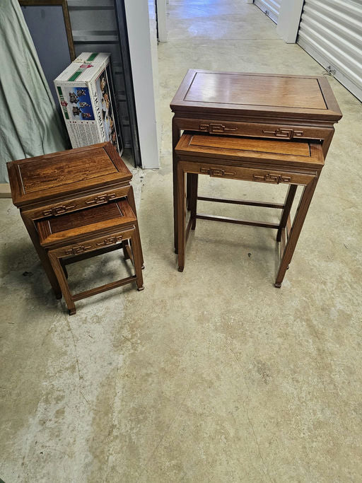 A set of three wooden side tables in a storage area, showcasing intricate detailing and varying heights, with one partially hidden behind a box.
