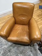 A worn, brown leather armchair with visible scratches and creases, situated on a patterned rug with wooden flooring in the background.
