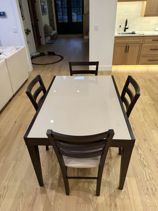 A modern dining table with four wooden chairs sits on a hardwood floor, surrounded by a cozy interior featuring a doorway and kitchen area.