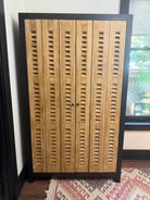 A wooden cabinet with a slatted design featuring four doors and black handles, positioned on a patterned rug near a window.