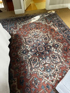 A richly patterned Persian rug in shades of red, blue, and cream, positioned on a light-colored floor, partially covered by a white blanket.