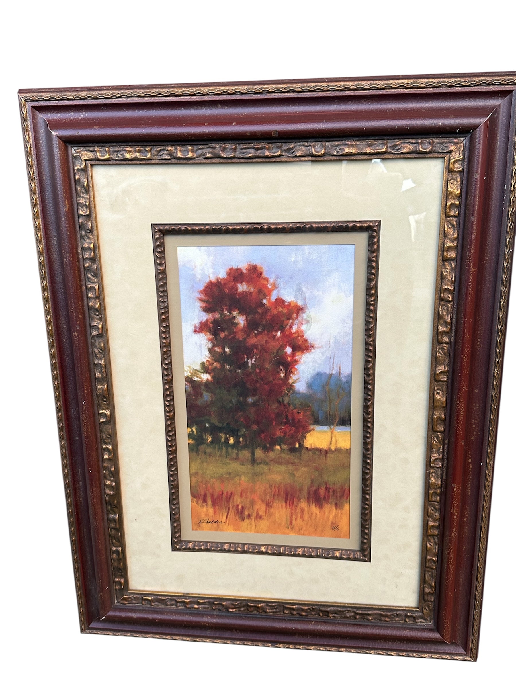 A framed painting features vibrant autumn trees in shades of red and orange, set against a soft blue sky and distant fields.