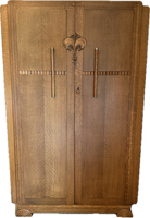 Art deco-style wooden cabinet with intricate grain patterns, featuring two doors, metal handles, and a decorative center motif.