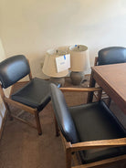 Two beige lamps with a "SAVE" sign sit beside a wooden table, flanked by two black chairs on carpeted flooring.