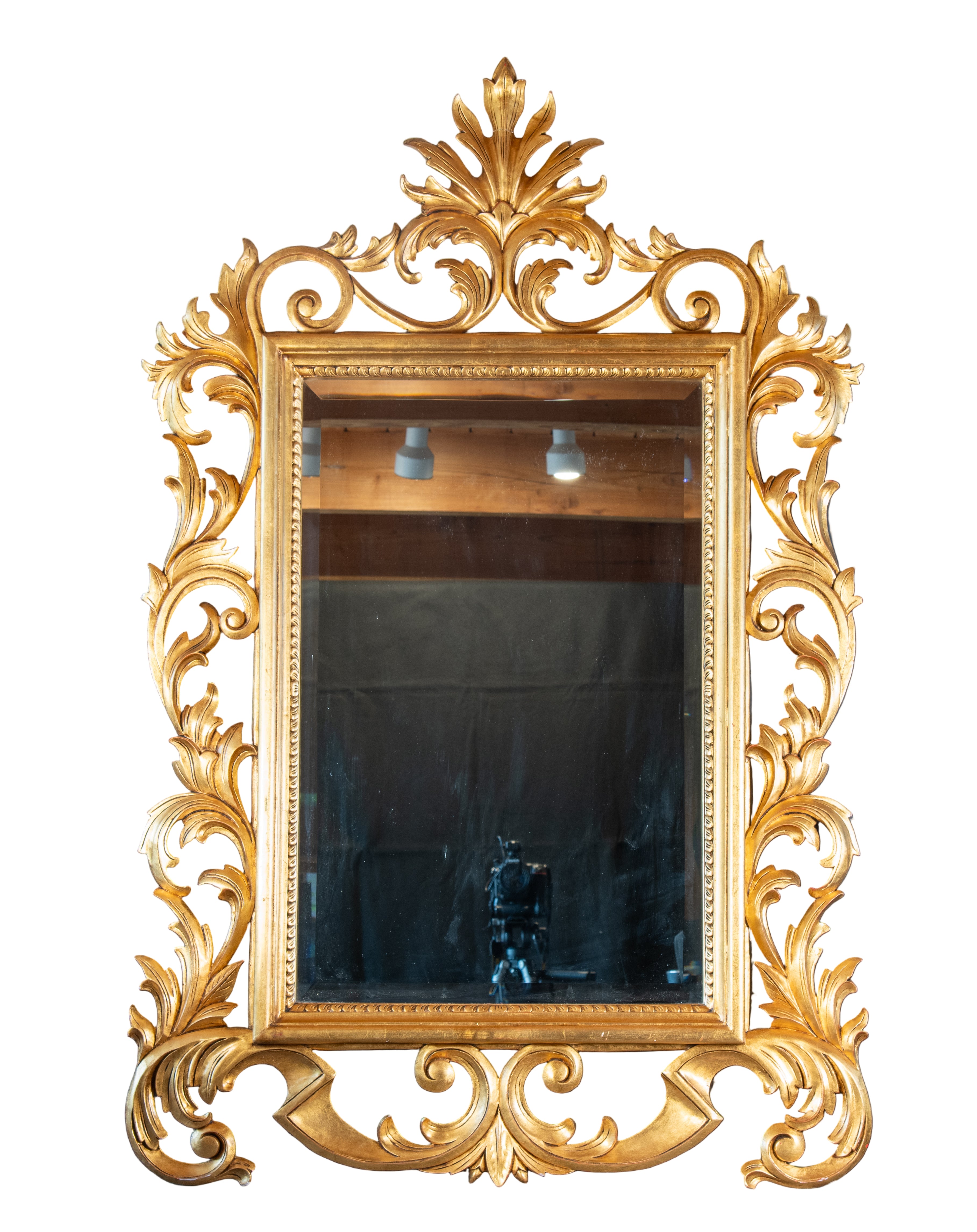 A large, ornate gold-framed mirror with intricate leaf and scroll designs reflects light and adds elegance to the space. Mounted above a fireplace.