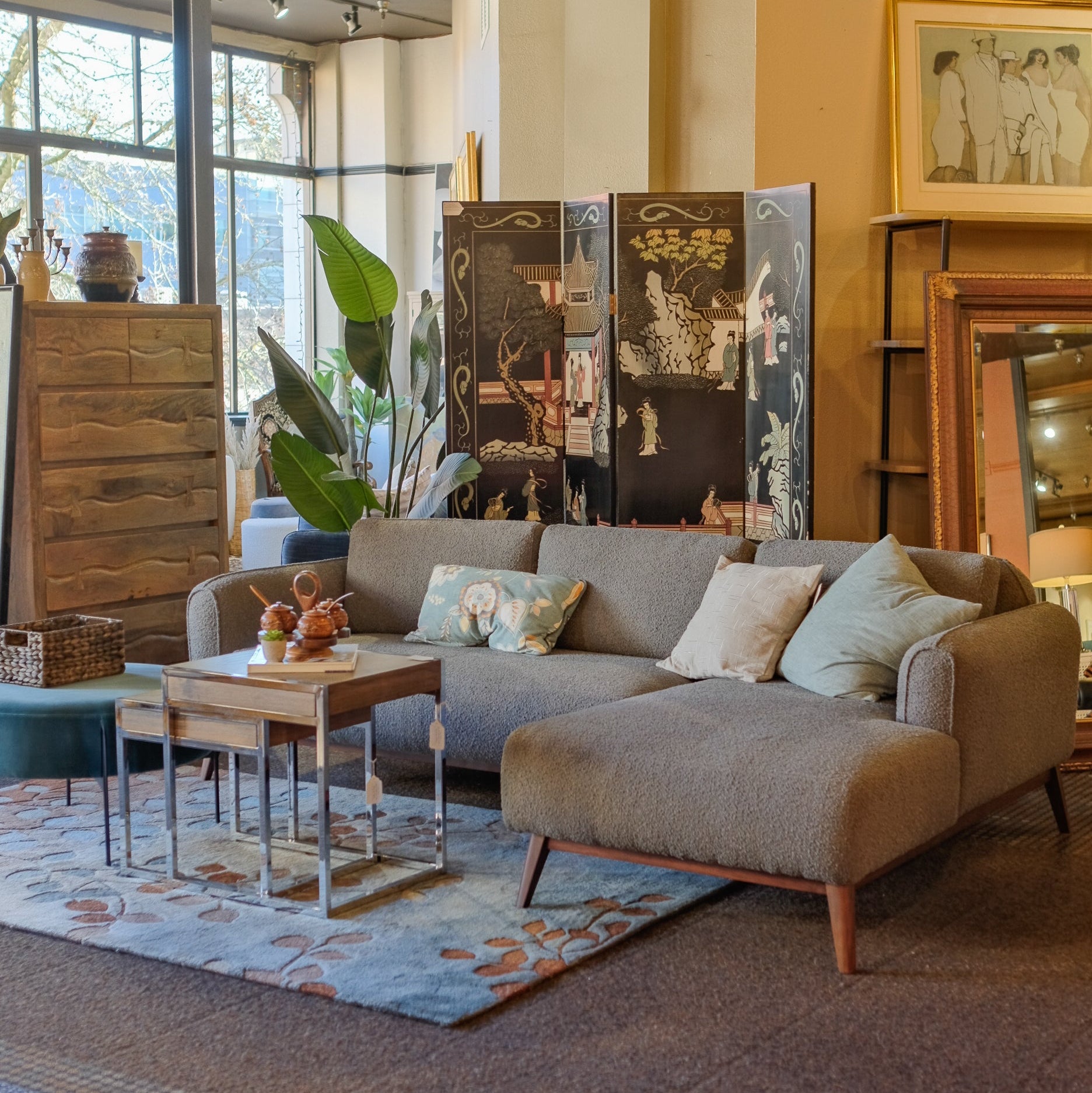 A modern grey textured sectional sofa with wooden legs and decorative pillows in the Tacoma Furniture Consignment showroom, featuring a live edge coffee table and vintage home decor.