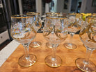 A collection of elegant, hand-painted glass goblets featuring floral designs and gold accents, arranged on a wooden surface.