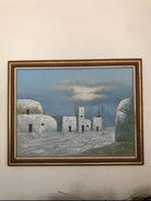 A framed painting depicts several white, rocky buildings under a blue sky with clouds, suggesting a tranquil, desert-like landscape.