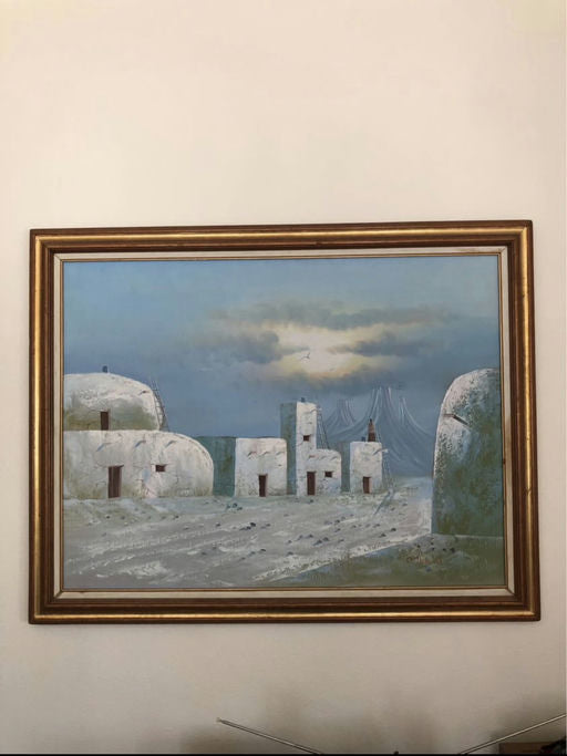 A framed painting depicts several white, rocky buildings under a blue sky with clouds, suggesting a tranquil, desert-like landscape.