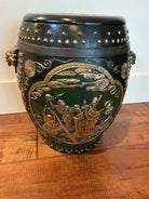 A decorative pot featuring intricate gold and green designs, depicting figures on water. The surface has a textured finish with metallic accents.