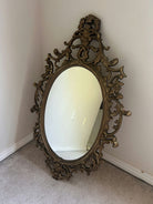 An ornate, vintage mirror with an elegant gold frame rests against a wall on soft carpet, reflecting the room's subtle details.