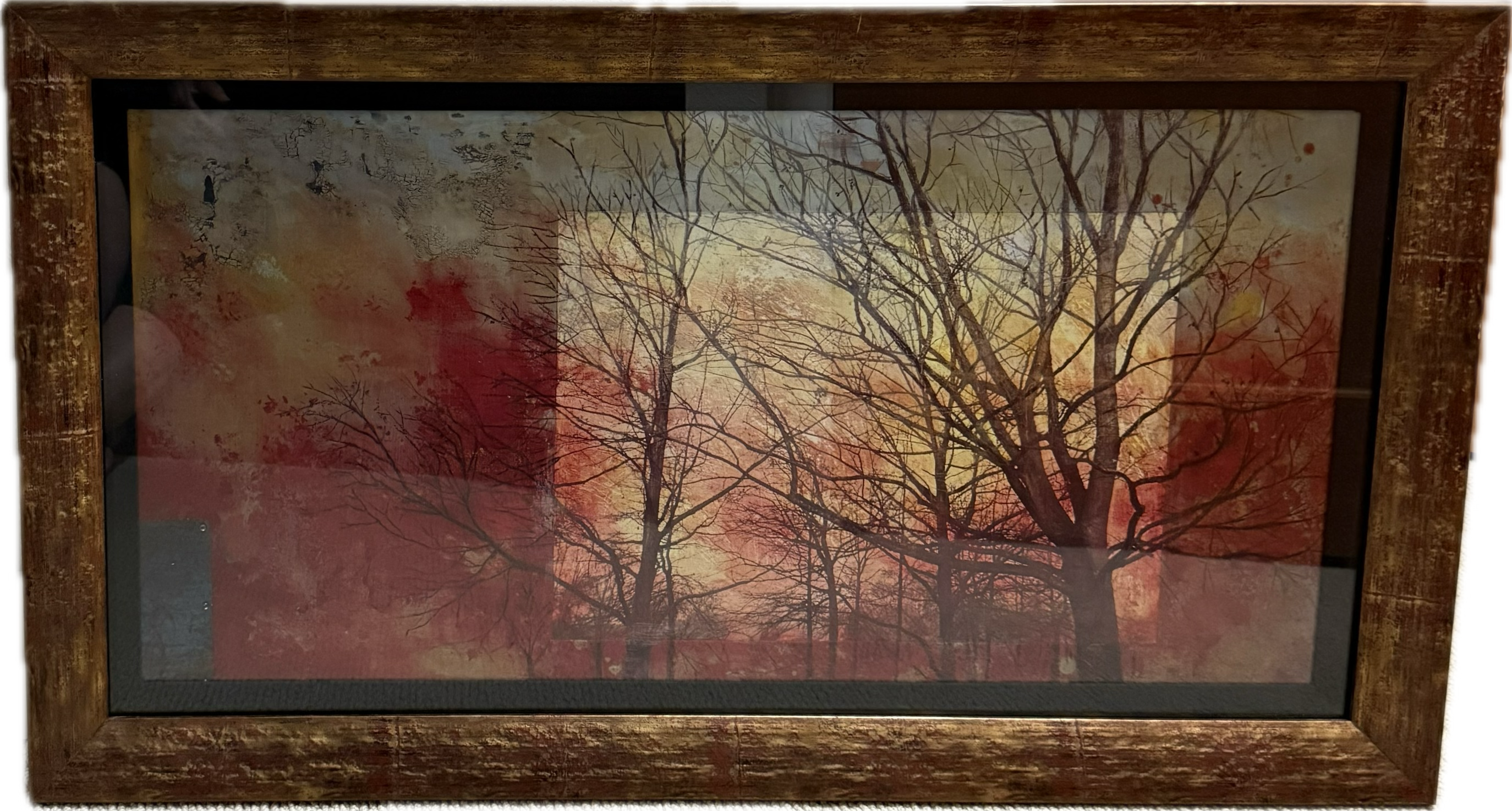 Framed artwork featuring silhouetted trees against a warm, gradient background of reds and yellows, evoking a serene sunset atmosphere.