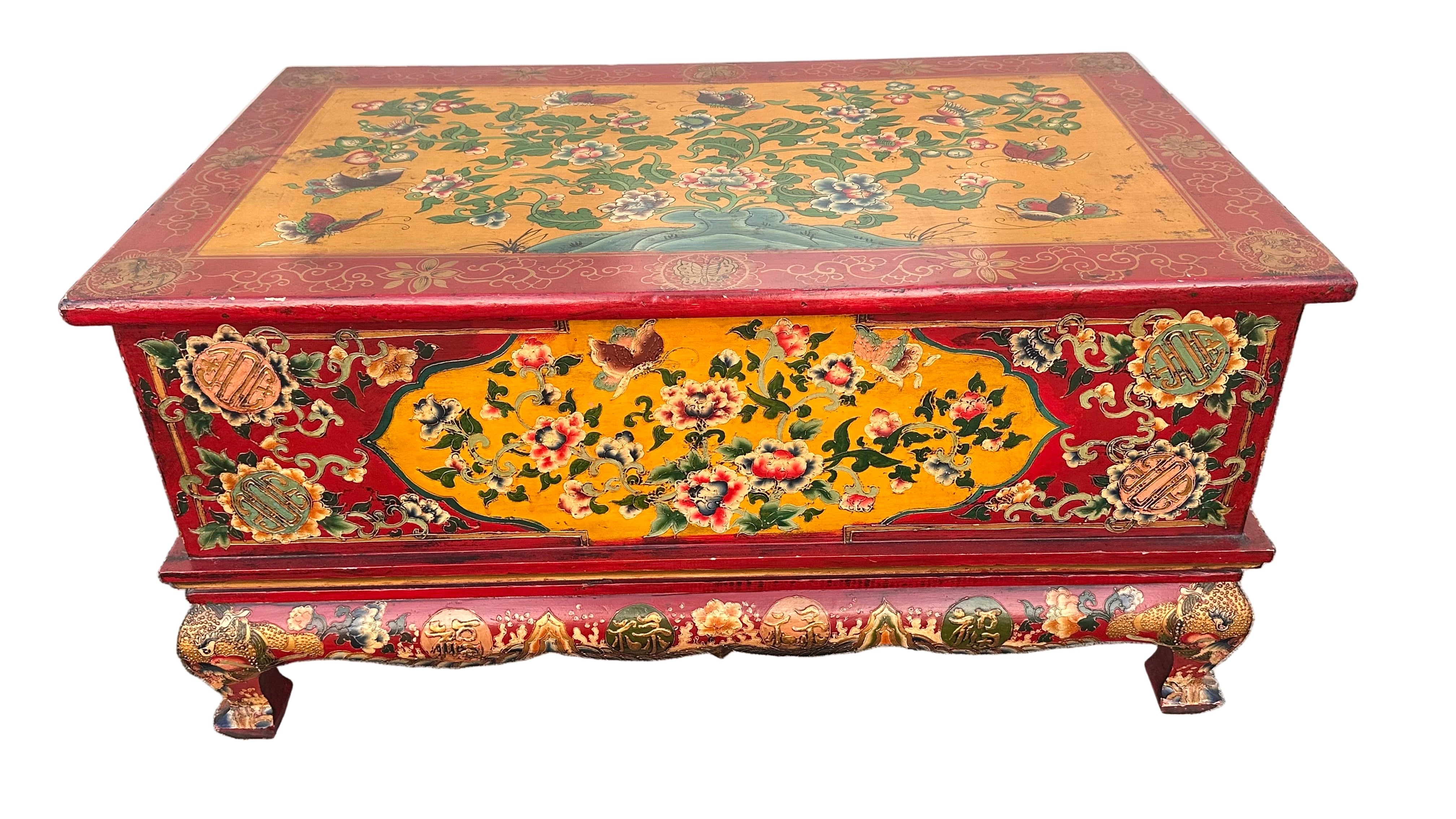 A colorful, antique wooden chest featuring intricate floral and animal designs in red, yellow, and green, resting on a stone surface.