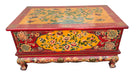 A colorful, antique wooden chest featuring intricate floral and animal designs in red, yellow, and green, resting on a stone surface.