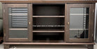 A wooden storage unit with clear glass doors, revealing three open shelving spaces. Reflections visible in the glass, showcasing a modern design.